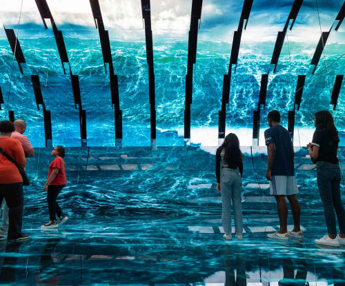 Guests standing in an exhibition space watching large video display of ocean waves