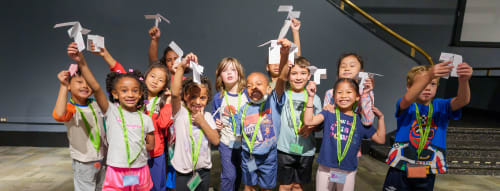 Group of young children holding up paper airplanes