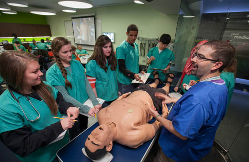 Students and instructor in medical scrubs discussing medical mannikin on table