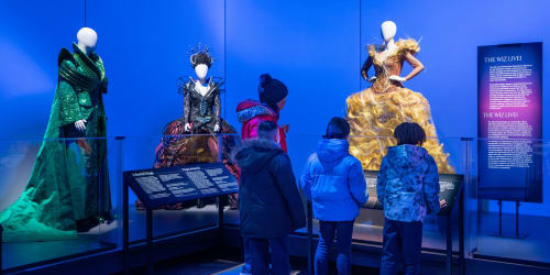 A group of visitors gather around a collection of extravagent costumes from 'The Wiz'. 