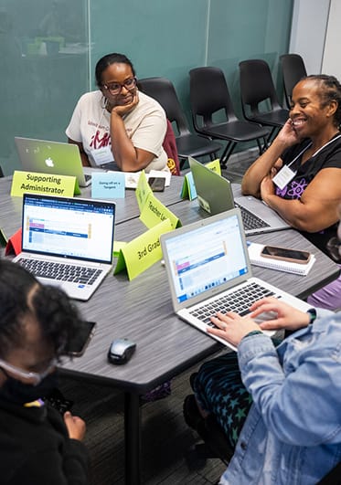 Smiling teachers seated around a table with laptops