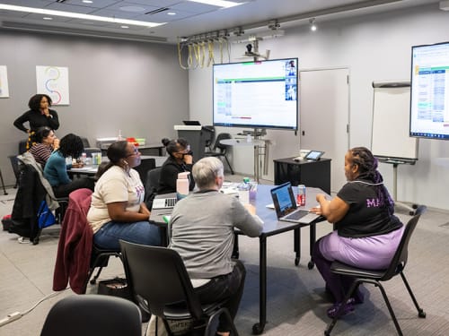 Teacher workshop discussing slides shown on video monitors