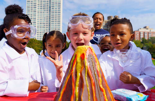 Young students in lab gear reacting to an outdoor "volcano" experiment