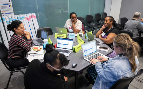 Smiling teachers seated around a table with laptops